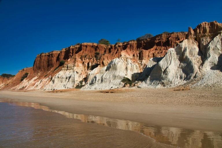 Scenic view of colorful cliffs on Algarvia Beach, Azores, Portugal, under a clear blue sky.