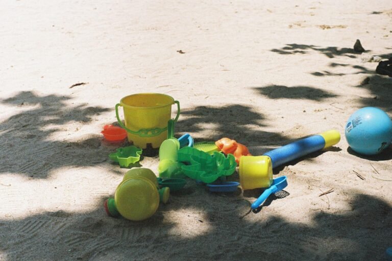 Brightly colored beach toys scattered on sandy shore under tree shadows.
