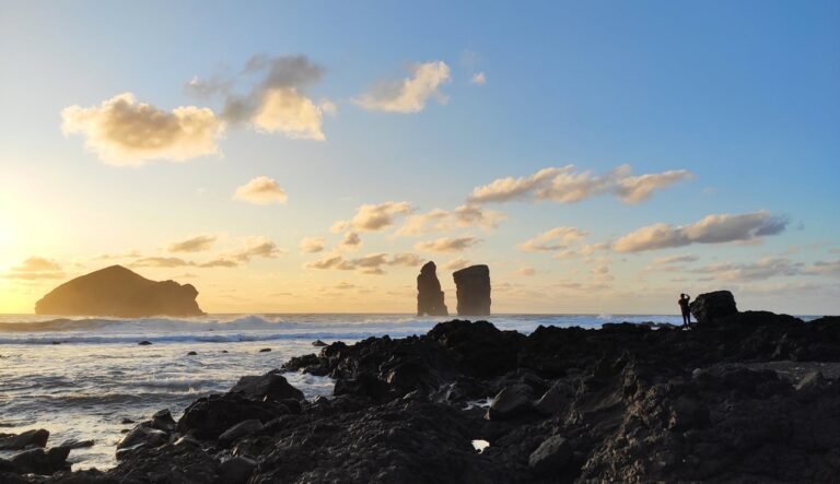 Stunning sunset at Mosteiros Beach, Açores, Portugal, with basalt rock formations and a lone photographer.